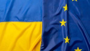 Das Bild zeigt zwei ineinander überlaufende Flaggen: auf der linken Seite die blau- gelbe ukrainische Flagge und auf der rechten Seite die EU-Flagge (gelber Sternenkreis auf dunkelblauem Hintergrund). 