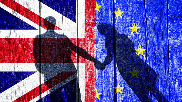 Auf dem Bild sieht man auf der einen Hälfte die Flagge des Vereinigten Königreichs, auf der anderen Hälfte die Flagge der EU. Auf die Flaggen fällt je ein Schatten von einer Dame und einem Herrn, die Händchen halten.