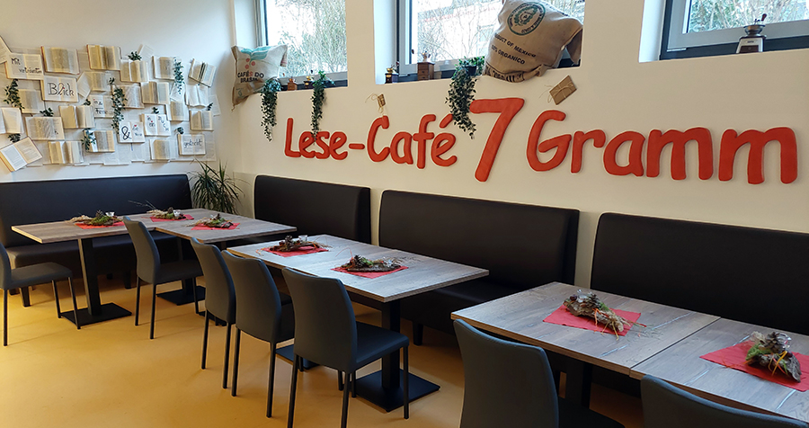 Tische und Stühle im Innenraum des Cafès; an der Außenwand steht in roter Schrift Lesecafé 7 Gramm