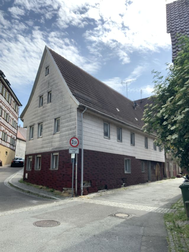 Das Bild zeigt ein Haus, das an einer kleinen Straße mit leichter Steigung liegt. Vor dem Haus steht ein "Anlieger frei"-Schild. 