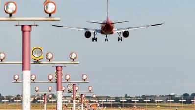 Ein Flugzeug befindet sich im Landflug, im Vordergrund sieht man Positionslichter entlang der Landebahn