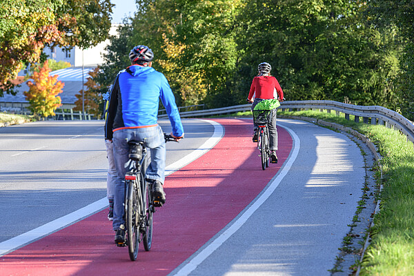 Symbolbild Radweg Zwei Fahrradfahrer fahren auf einem rot gekennzeichneten Radweg. man sieht sie von hinten