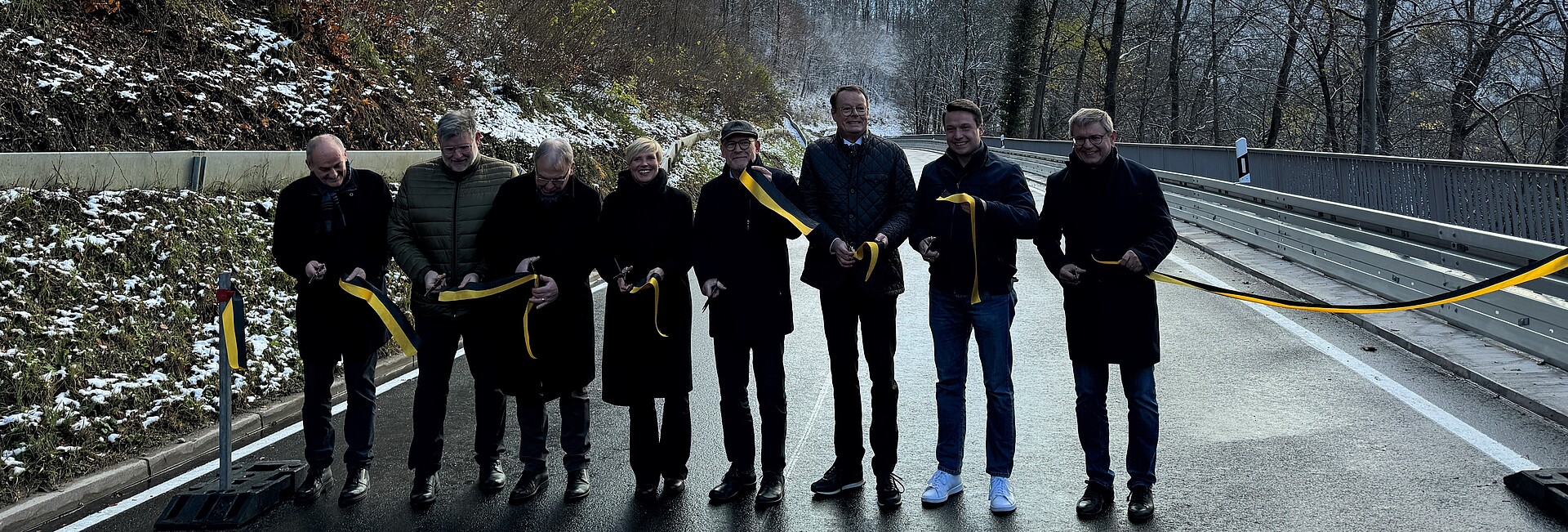 Eine Gruppe von Honoratioren steht auf der Straße nebeneinander und schneidet zur Freigabe ein Band durch. 