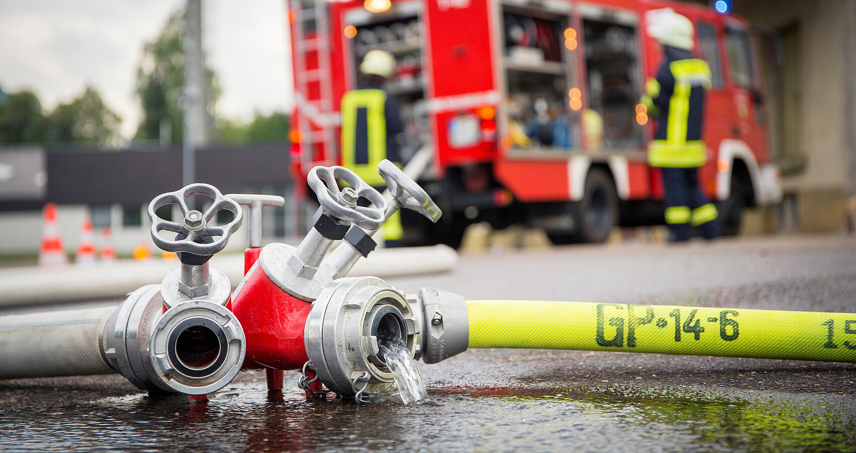 Bild zeigt Feuerwehrschlauch mit Feuerwehrfahrzeug im Hintergrund