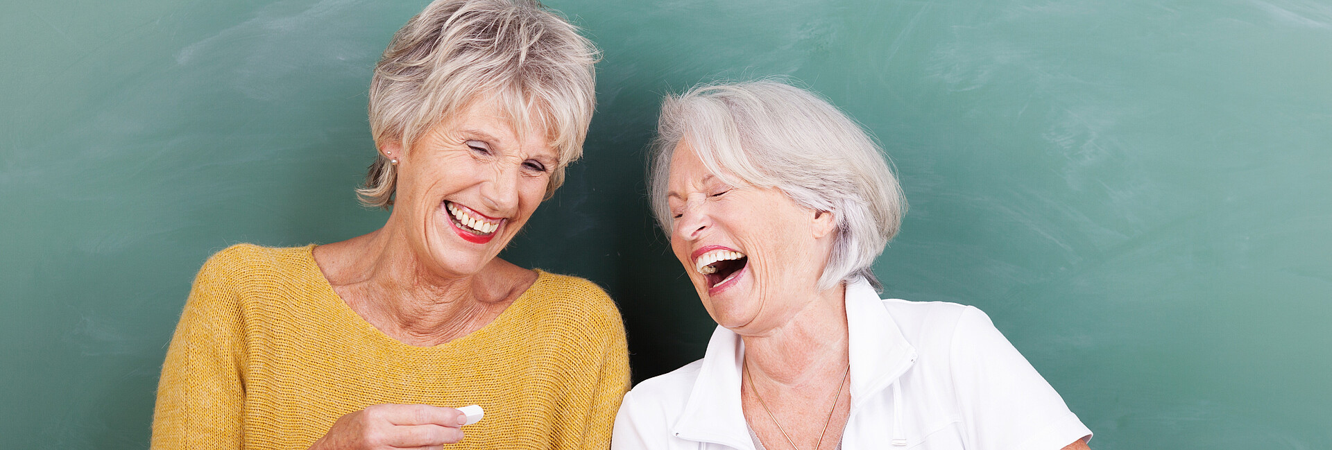 Lachende Seniorinnen vor einer Schultafel