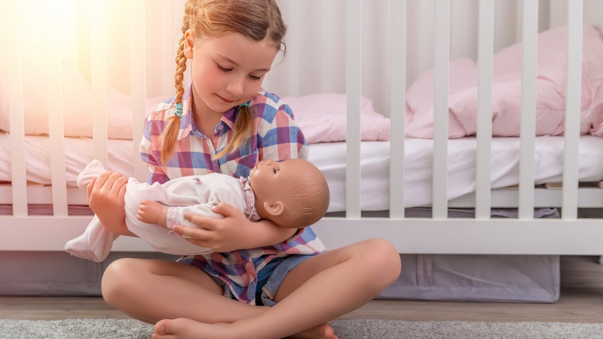 Ein Mädchen spielt mit ihrer Puppe vor dem Kinderbett
