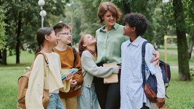 Eine Erzieherung steht mit vier Jugendlichen in einem Park
