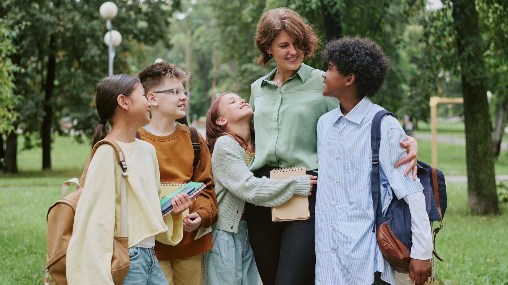 Eine Erzieherung steht mit vier Jugendlichen in einem Park