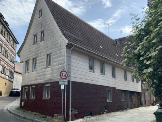 Das Bild zeigt ein Haus, das an einer kleinen Straße mit leichter Steigung liegt. Vor dem Haus steht ein "Anlieger frei"-Schild. 