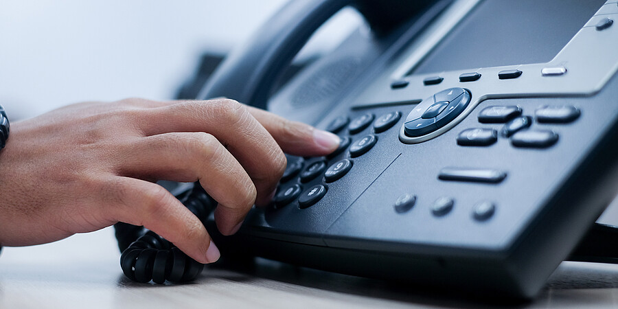 Eine Hand tippt eine Telefonnummer auf einem schwarzen Telefonapperat ein