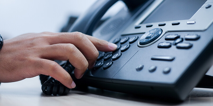 Eine Hand tippt eine Telefonnummer auf einem schwarzen Telefonapperat ein
