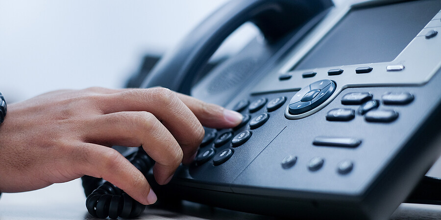 Eine Hand tippt eine Telefonnummer auf einem schwarzen Telefonapperat ein
