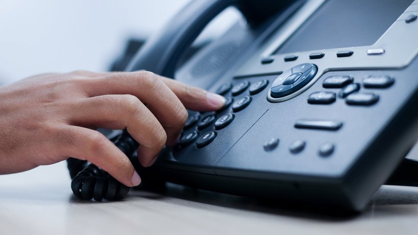 Eine Hand tippt eine Telefonnummer auf einem schwarzen Telefonapperat ein