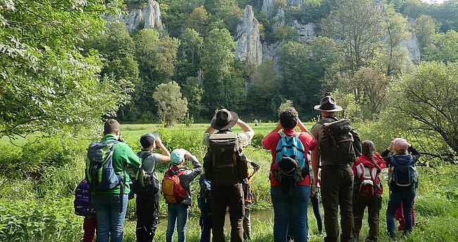 Wandergruppe im Biosphärengebiet Schwäbische Alb, die mit Ferngläsern auf einen Felsen blickt
