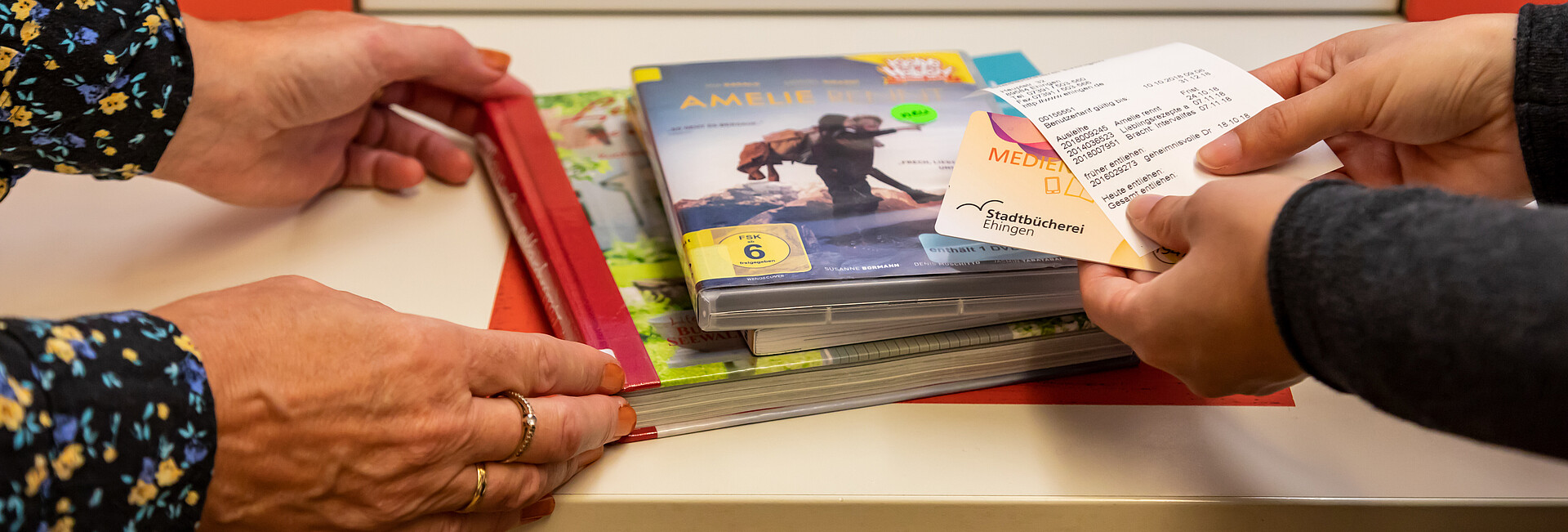 Vier Hände halten CDs und Bücher an den Selbstverbucher der Stadtbücherei Ehingen an der Donau 
