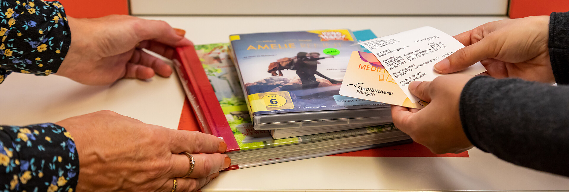 Vier Hände halten CDs und Bücher an den Selbstverbucher der Stadtbücherei Ehingen an der Donau 