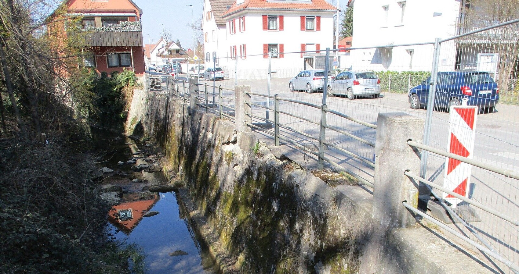 Das Bild zeigt die Stützwand entlang der L 382 und den Gewässerlauf am Eierbach in Pfullingen; man sieht Häuser und parkende Autos entlang der Friedrichstraße