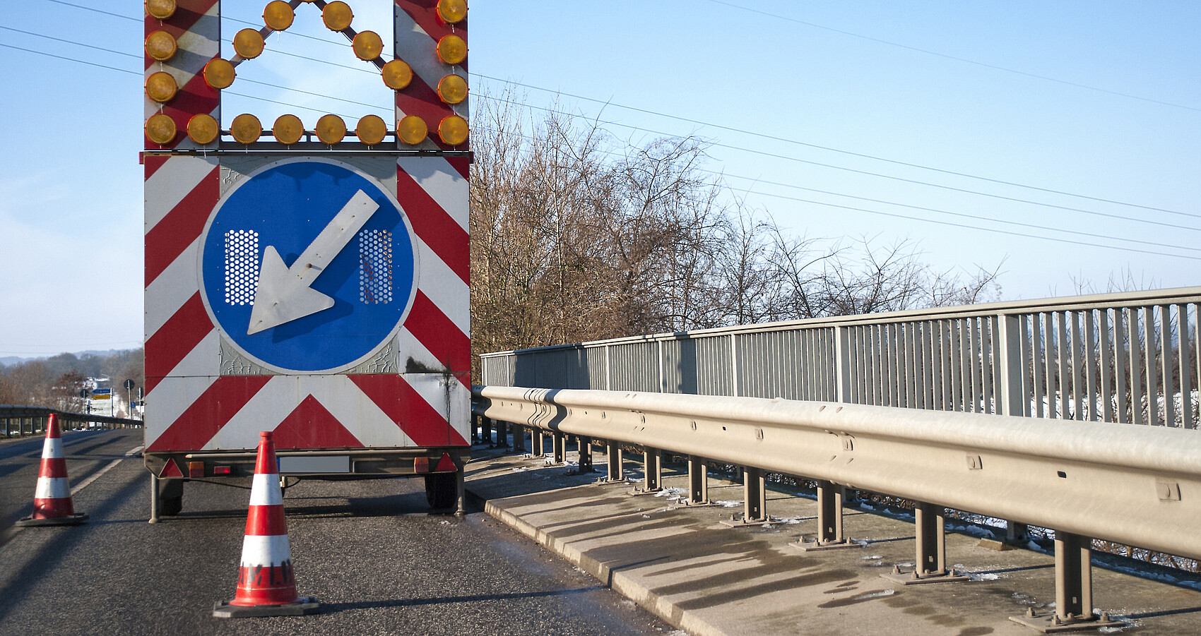 Baustelle auf einer Brücke mit Baustellenfahrzeug und Warnschild, Fahrbahnverengung