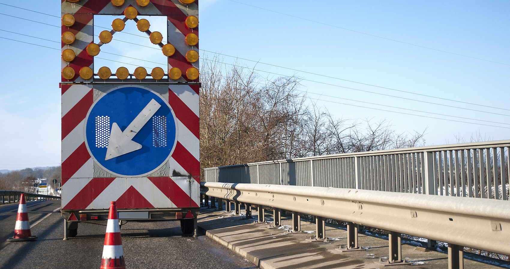 Baustelle auf einer Brücke mit Baustellenfahrzeug und Warnschild, Fahrbahnverengung