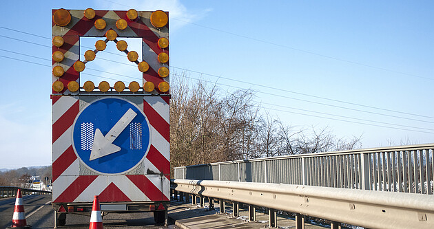 Baustelle auf einer Brücke mit Baustellenfahrzeug und Warnschild, Fahrbahnverengung