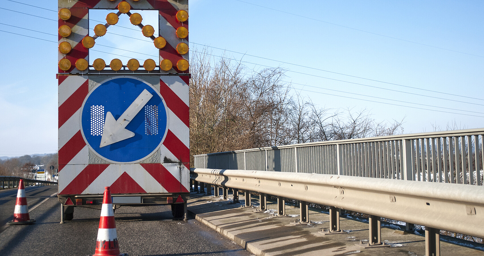 Baustelle auf einer Brücke mit Baustellenfahrzeug und Warnschild, Fahrbahnverengung