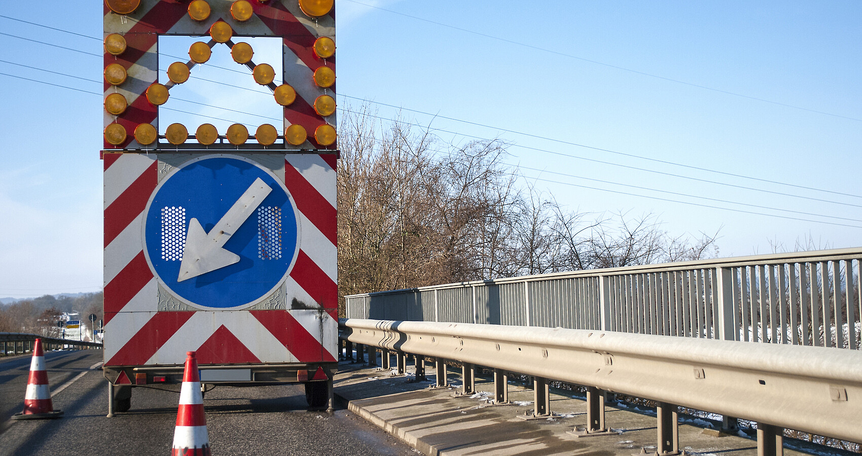 Baustelle auf einer Brücke mit Baustellenfahrzeug und Warnschild, Fahrbahnverengung