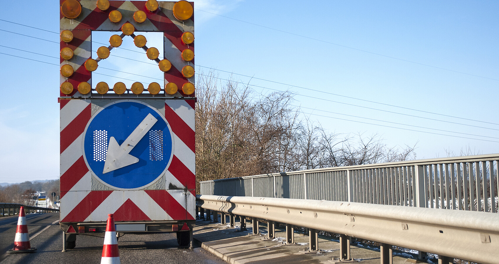 Baustelle auf einer Brücke mit Baustellenfahrzeug und Warnschild, Fahrbahnverengung