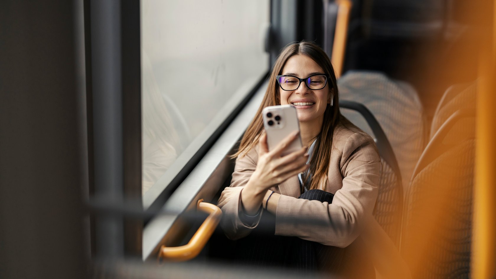 Eine junge Frau sitzt im Bud und blickt lächelnd auf ihr Handy.