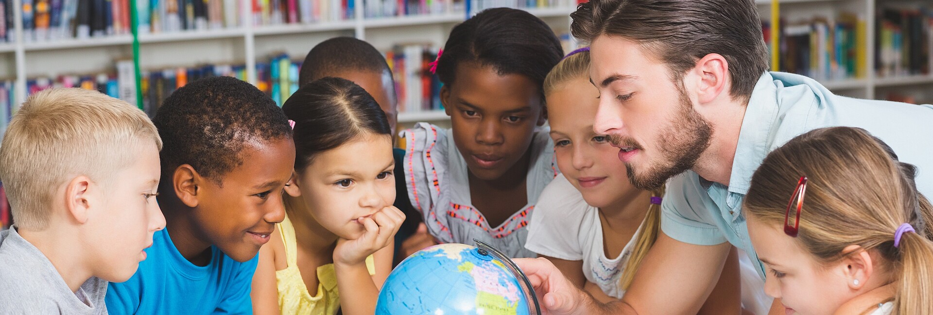 Ein Lehrer und mehrere Kinder sitzen um einen Globus