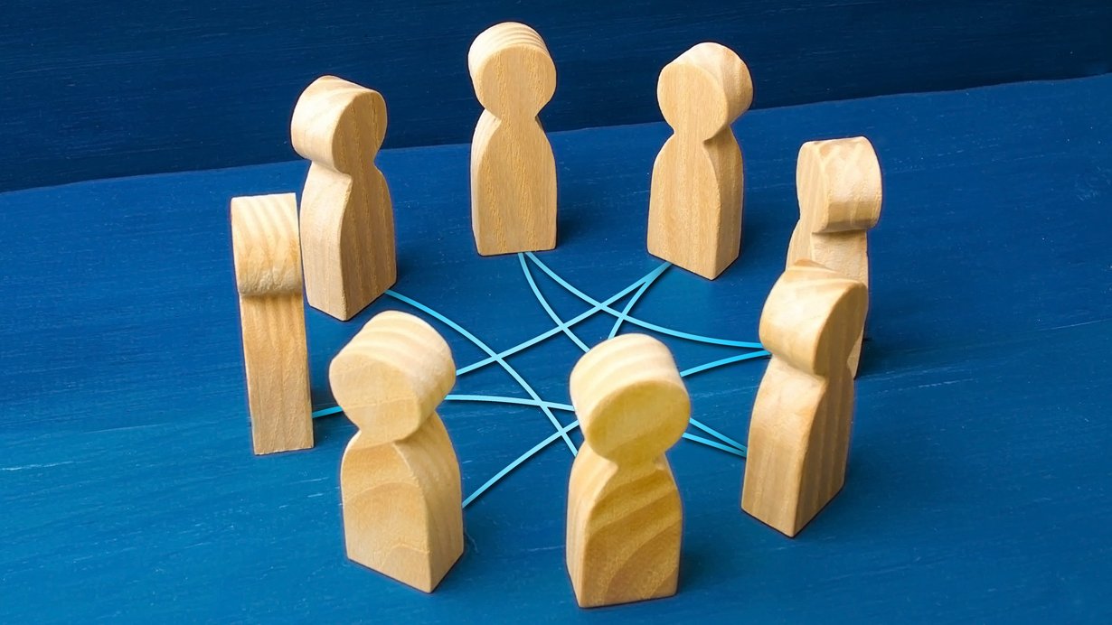 Acht Holzmännchen stehen auf einer blauen Fläche im Kreis und sind über Fäden verbunden.