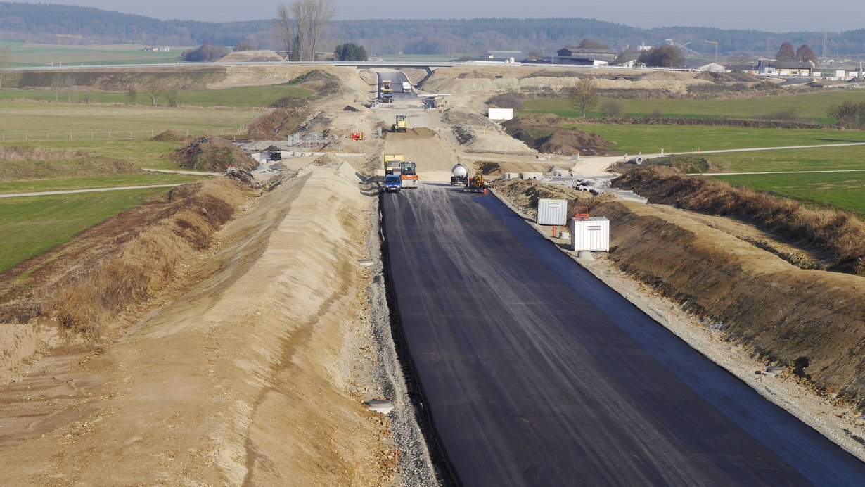 Blick von oben auf eine Straßenbaustelle mit Baufahrzeugen und Bauarbeitern