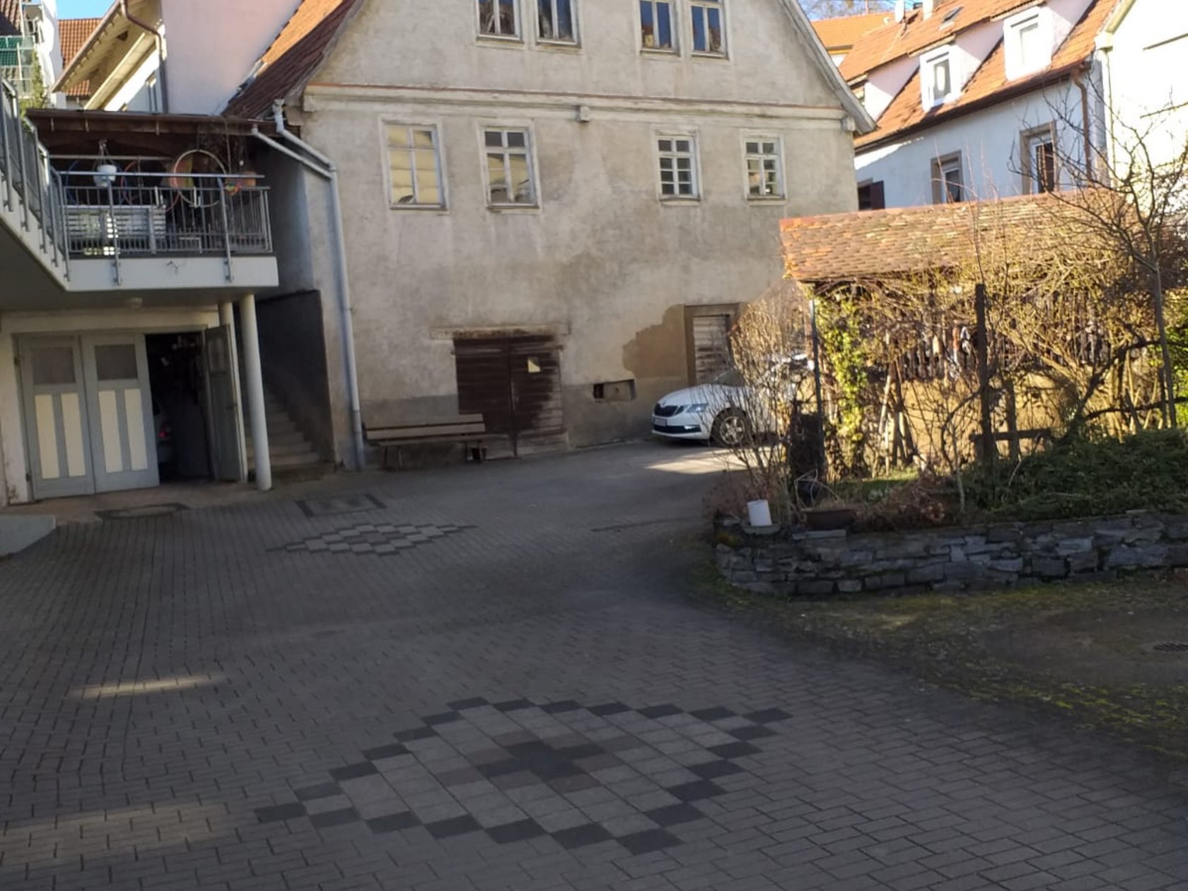 Das Bild zeigt die Seitenansicht eines Hauses. Vor dem Haus steht eine Bank. 