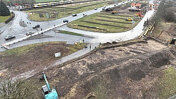 Ein Drohnenbild einer Kreuzung. Unten links sind ein Bagger und leere Gasleitungen zu sehen. An der Straße entlang sind viele Baumstümpfe. Im Hintergrund sind auf einer Wiese mehrere Steinhaufen zu sehen.
