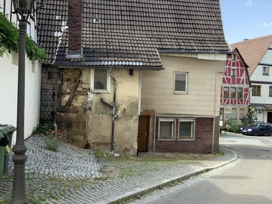 Seitenansicht eines älteren Hauses mit teilweise abgebröckelter Fassade und einer Tür.