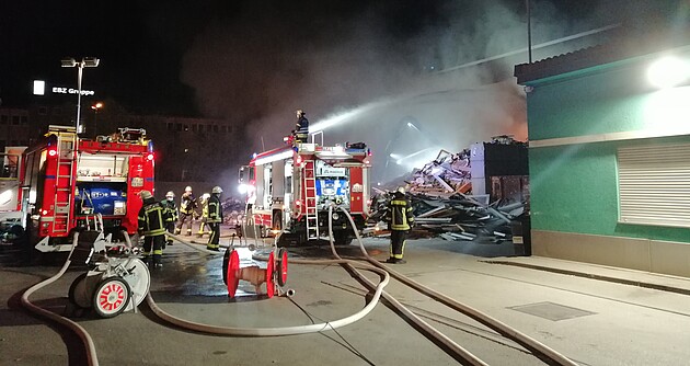 Das Foto zeigt zwei Feuerwehrfahrzeuge und mehrere Feuerwehrleute die mit Wasserschläuchen ein Gebäude löschen
