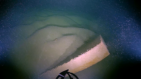 Eine Sandsteinplatte am Grund des Bodensees. Es handelt sich um verlorengegangene Ladung des hölzernen Lastsegelschiffs. Im Vordergrund Teil des ROV-Greifarms 