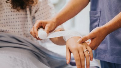 Eine Krankenschwester legt einer Frau einen Verband am Arm an