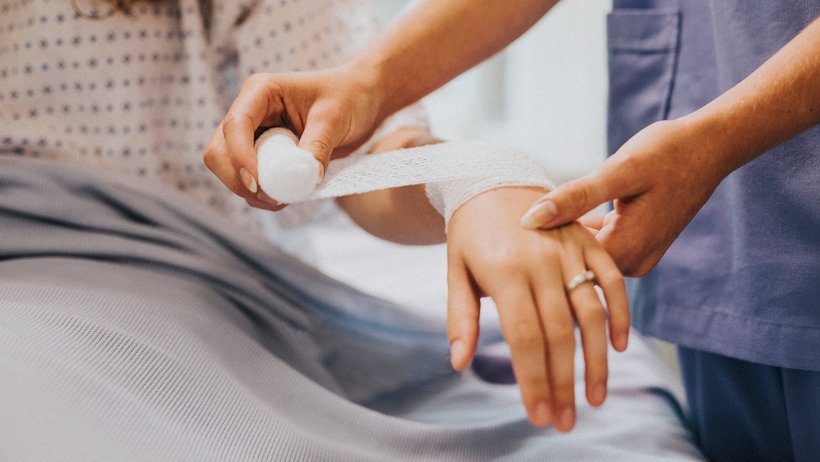 Eine Krankenschwester legt einer Frau einen Verband am Arm an