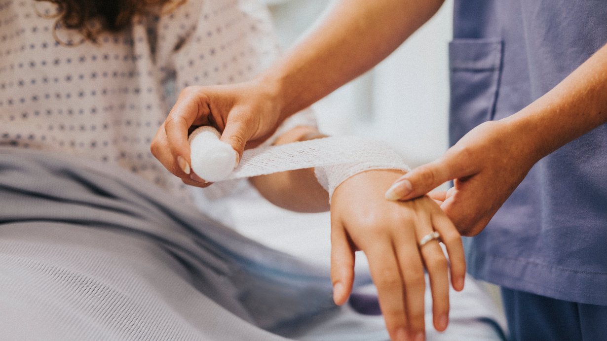 Eine Krankenschwester legt einer Frau einen Verband am Arm an