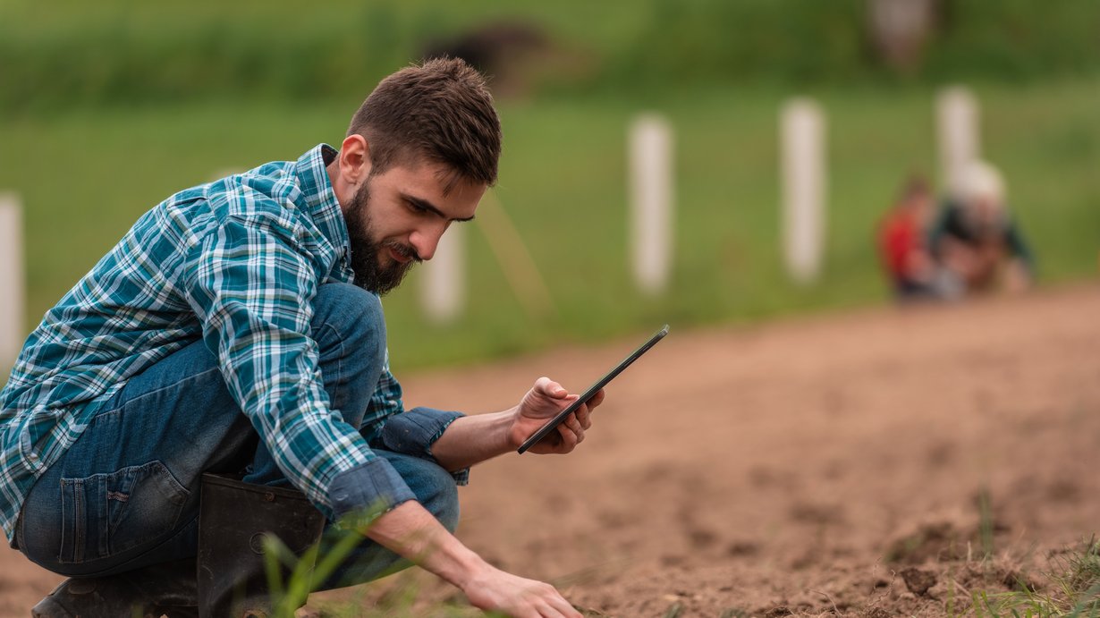 ein Landwirt kniet auf dem feld und prüft die aufgehende Saat. 