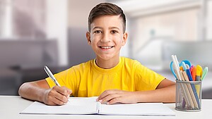 Lächelnder Schuljunge im gelben T-Shirt, der Hausaufgaben macht und am Tisch sitzt