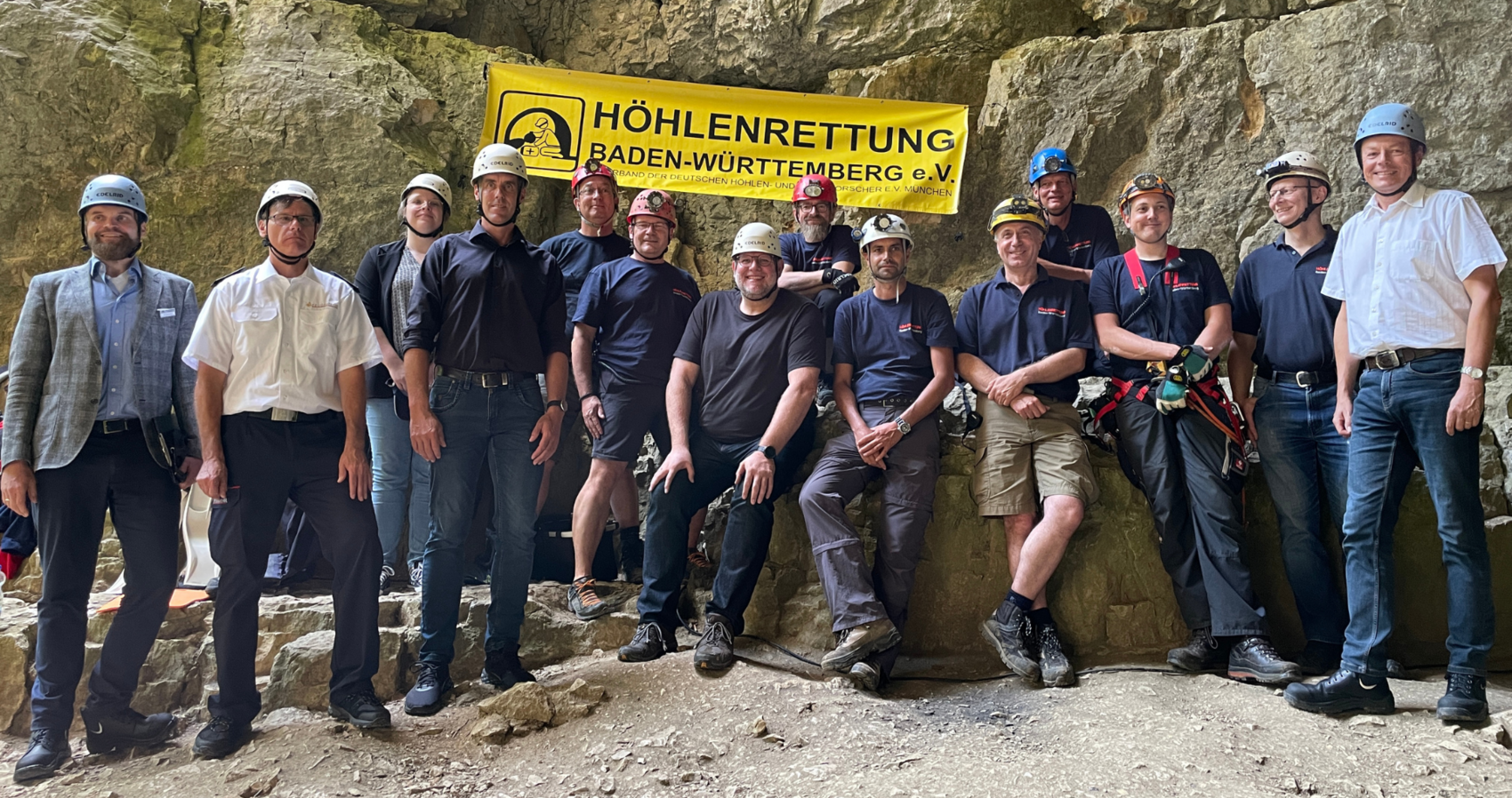 Das Gruppenfoto im Eingangsbereich der Falkensteiner Höhle zeigt Mitglieder der Höhlenrettung Baden-Württemberg e.V.. Auf der rechten Seite steht Herr Regierungspräsident Klaus Tappeser. Im oberen Bildbereich ist ein Banner mit dem Logo des Vereins an der Höhlenwand zu sehen.