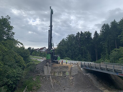 Juli 2025: Die Bohrpfähle für die Widerlager der neuen Brücke werden hergestellt. Ein Bohrgerät neben einer Brücke