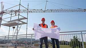 Zwei Baureferendare mit Karte vor Baukran