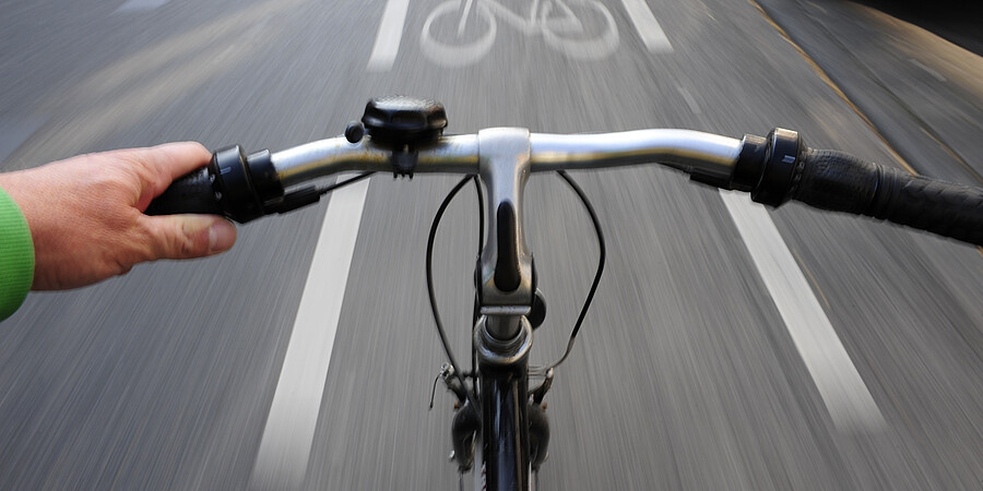 Blick über den Lenker:Fahrrad in schneller Fahrt auf einem Fahrradweg
