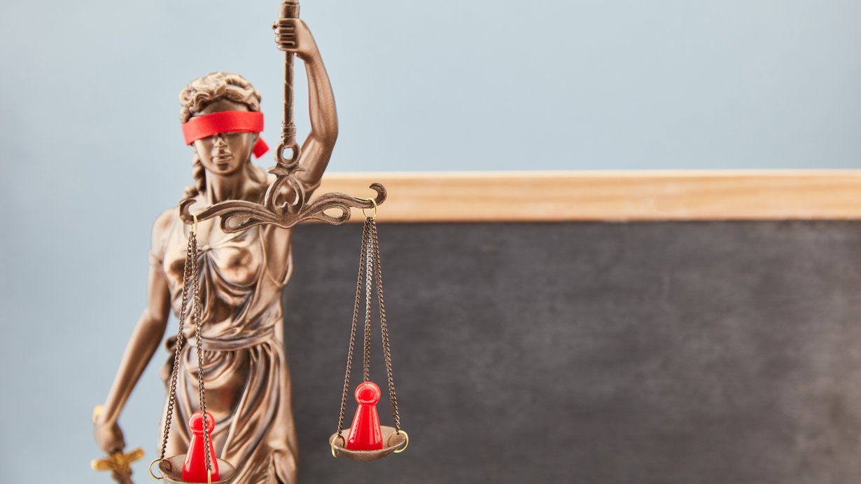 Justitia Bronze steht vor Tafel