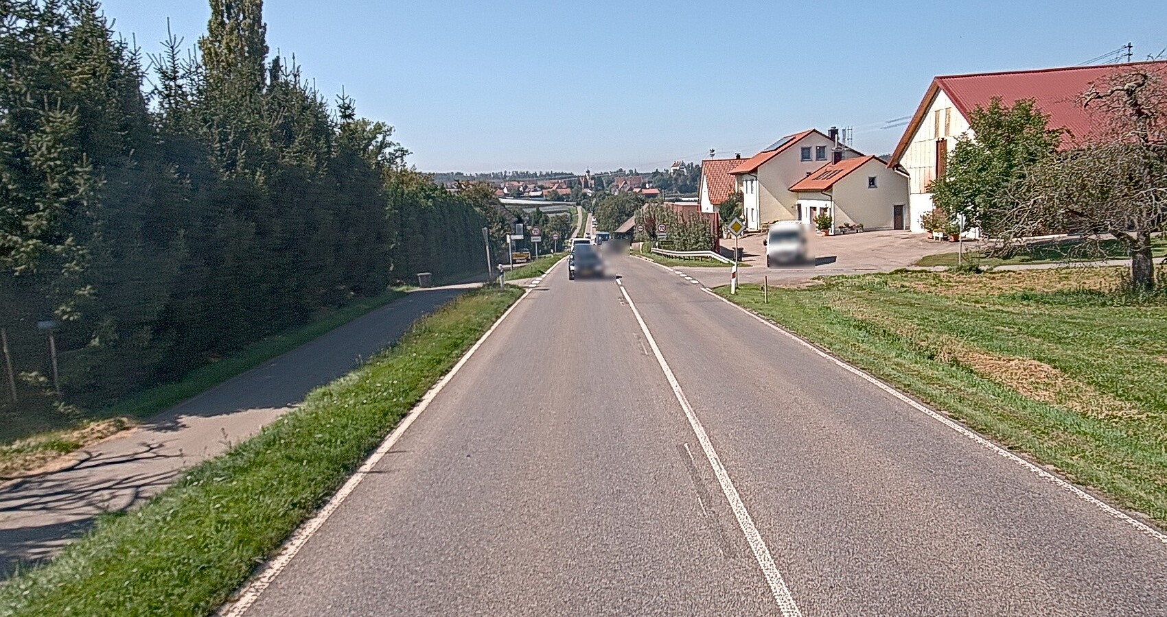 Das Foto zeigt eine Straße, die durch eine Ortschaft führt. Links sieht man Häuser