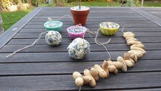 Auf einem Holztisch: Erdnusskette, Vogelfutter in 3 Silikonförmchen, Vogelfutter im Blumentopf, 2 Vogelfutterkugeln