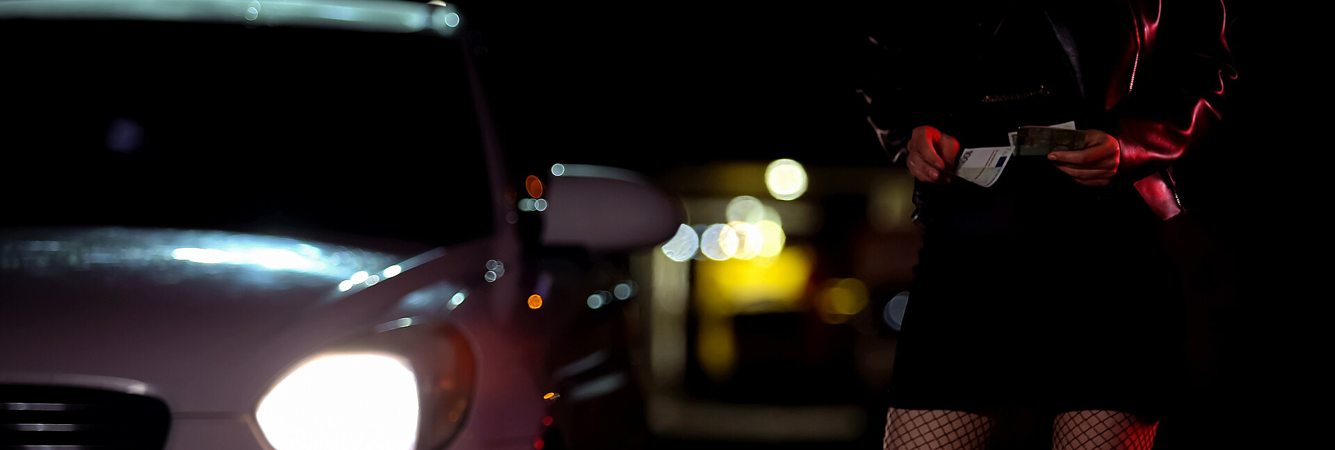 Prostituierte in Strüpfen mit Geldscheinen in der Hand neben einem Auto