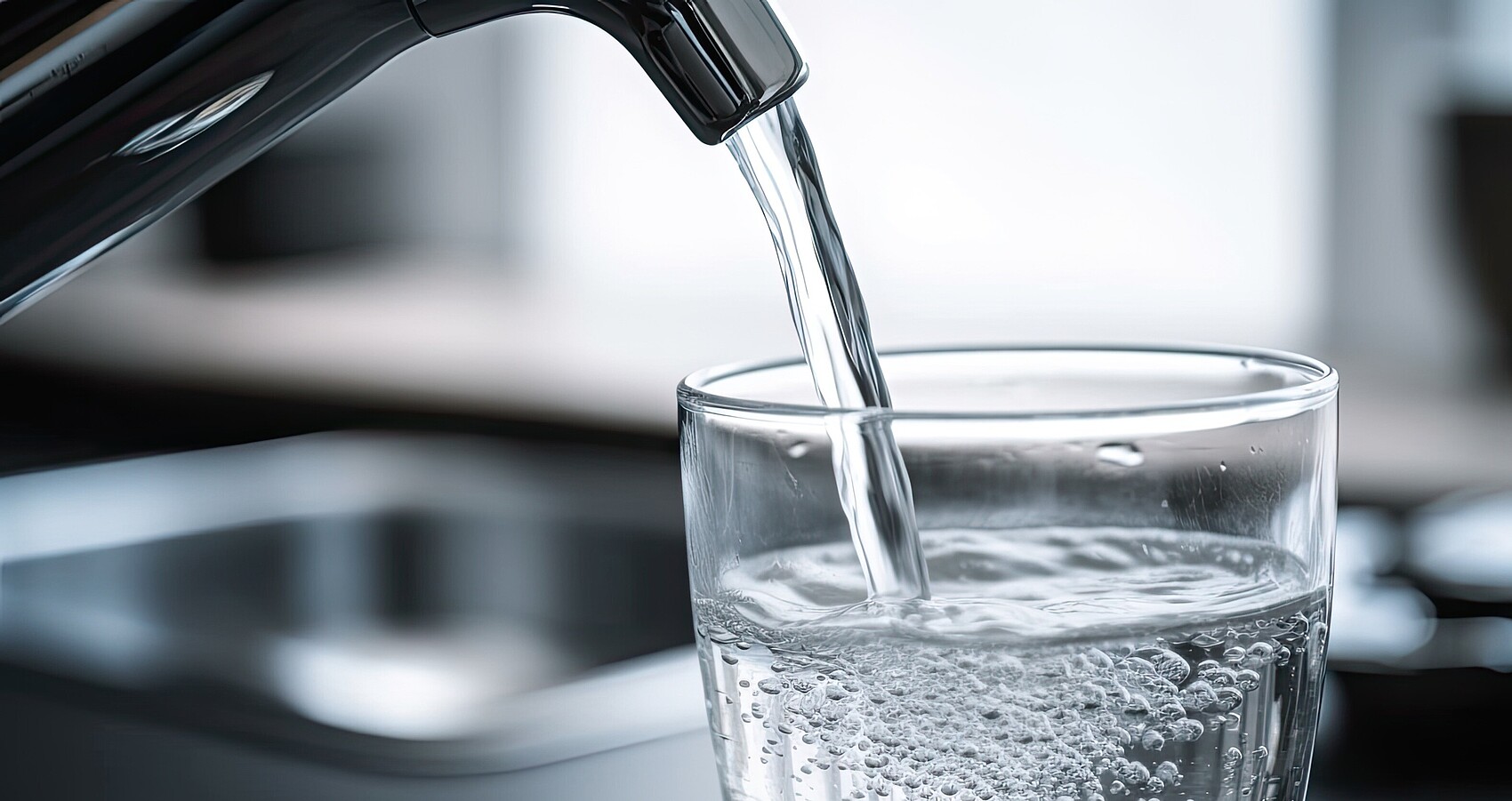 Trinkwasser fließt aus einer Küchenarmatur in ein Glas